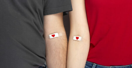 Blood donorship. Man in grey and woman in red T-shirt with hands taped patch after giving blood with red heart